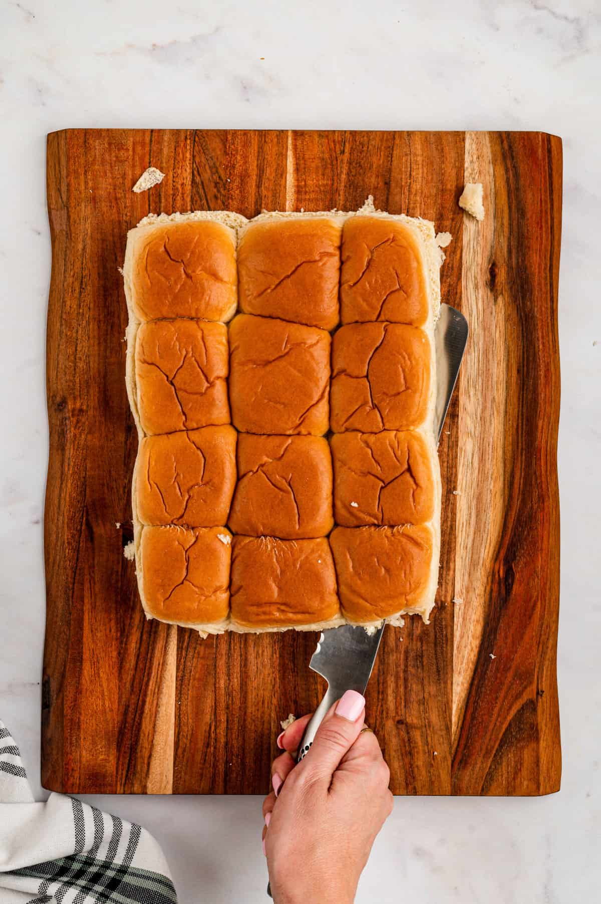 Slicing Hawaiian Rolls on a wooden cutting board for Pizza Sliders recipe