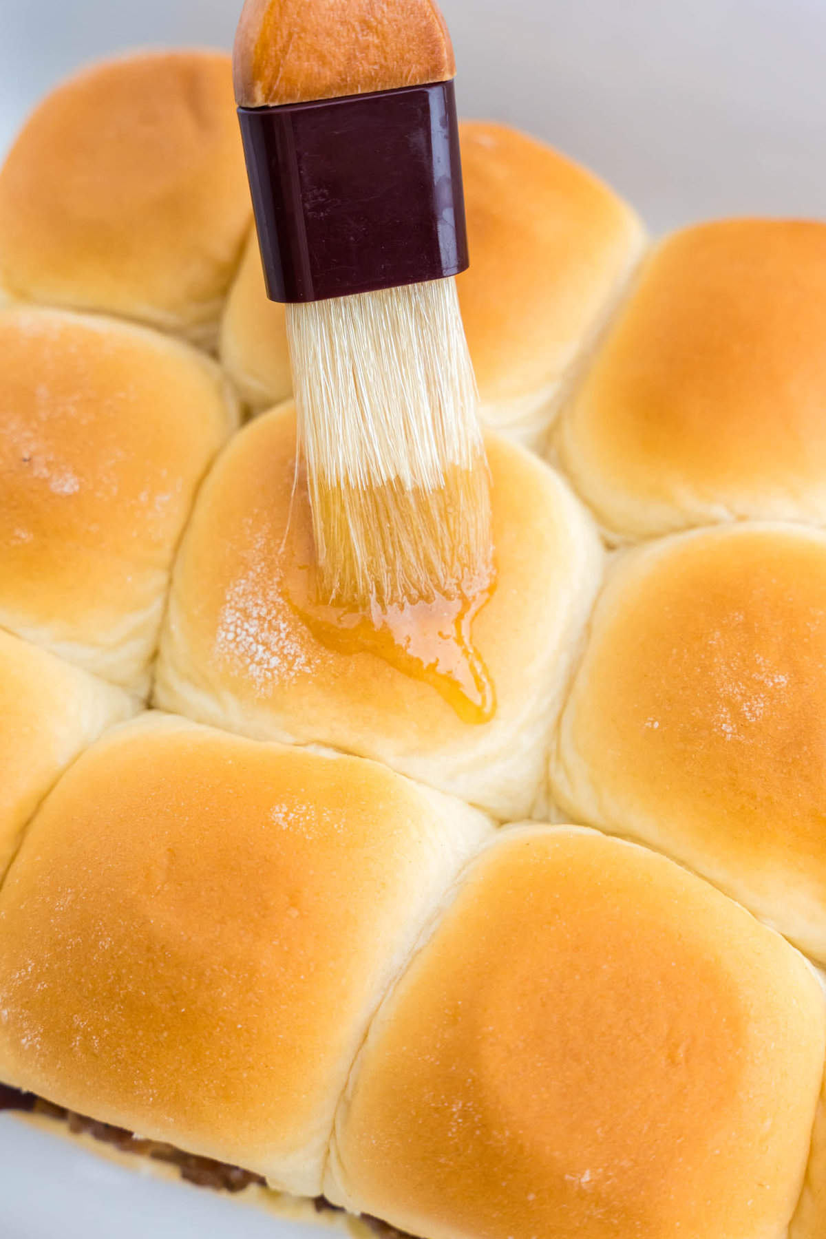 Brushing on seasoned butter mixture atop Hawaiian buns for Pulled Pork Sliders