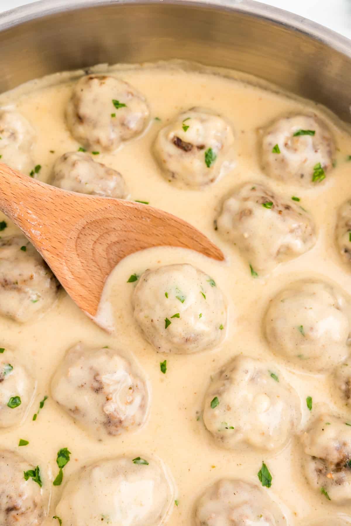 Wooden spoon scooping swedish meatball out of skillet