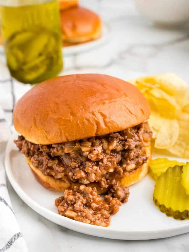 Large Batch Sloppy Joes recipe with meat on bun with chips and pickles on the side