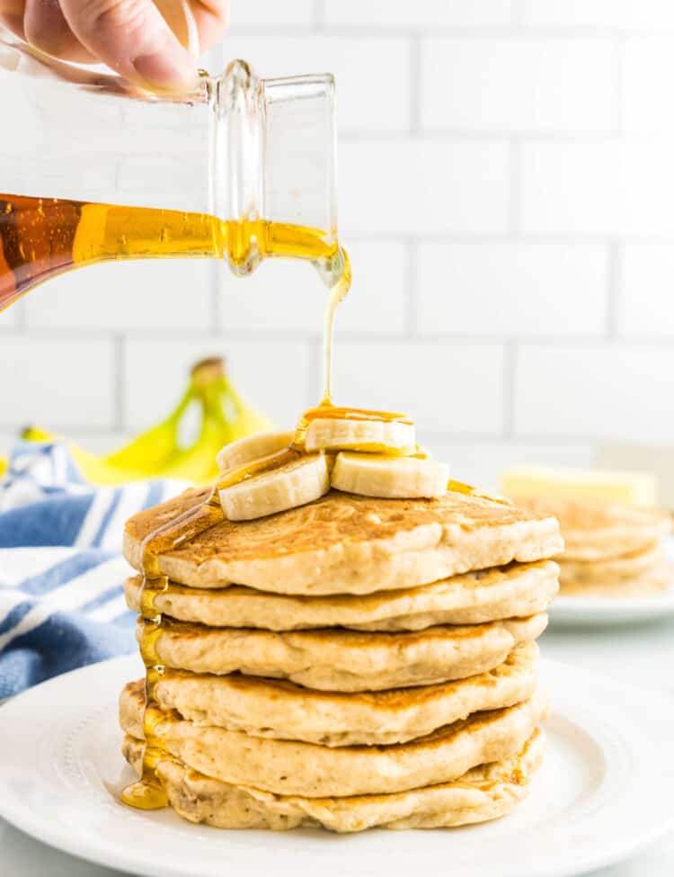 Pouring syrup on stack of banana pancakes