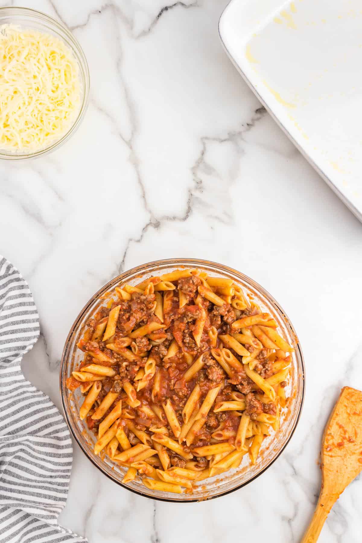Tossed ground beef mixture and cooked penne noodles in glass mixing bowl for Hamburger Casserole