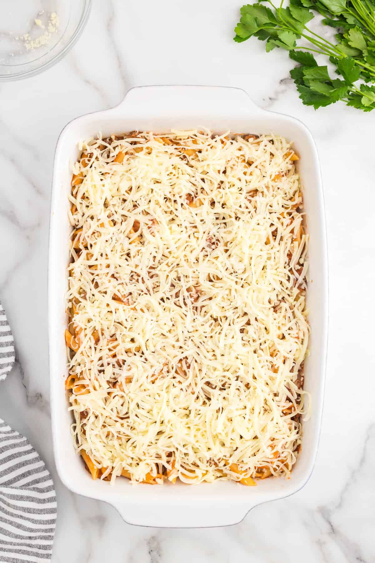 Topping casserole mixture with shredded cheese in baking dish for Ground Beef Casserole