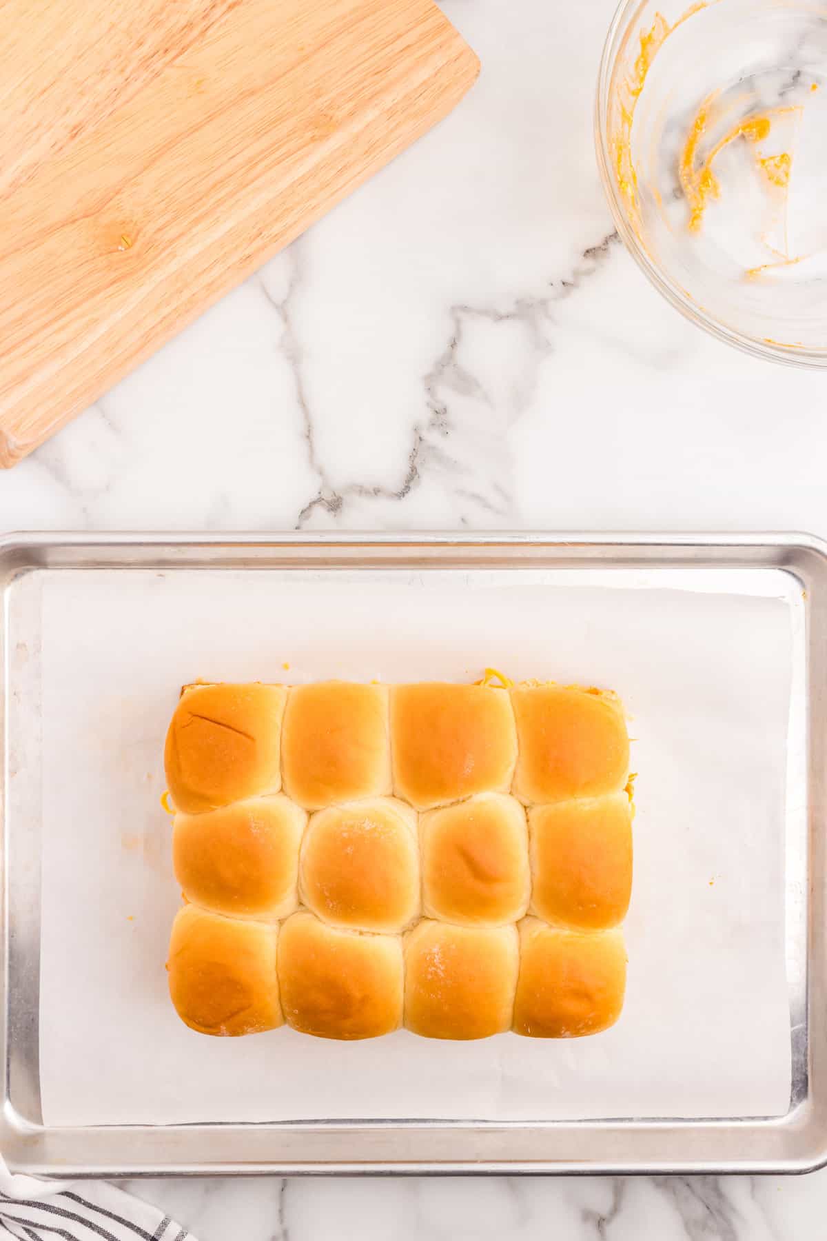 Topping cheese and buffalo chicken to hawaiian buns on parchment lined baking sheet