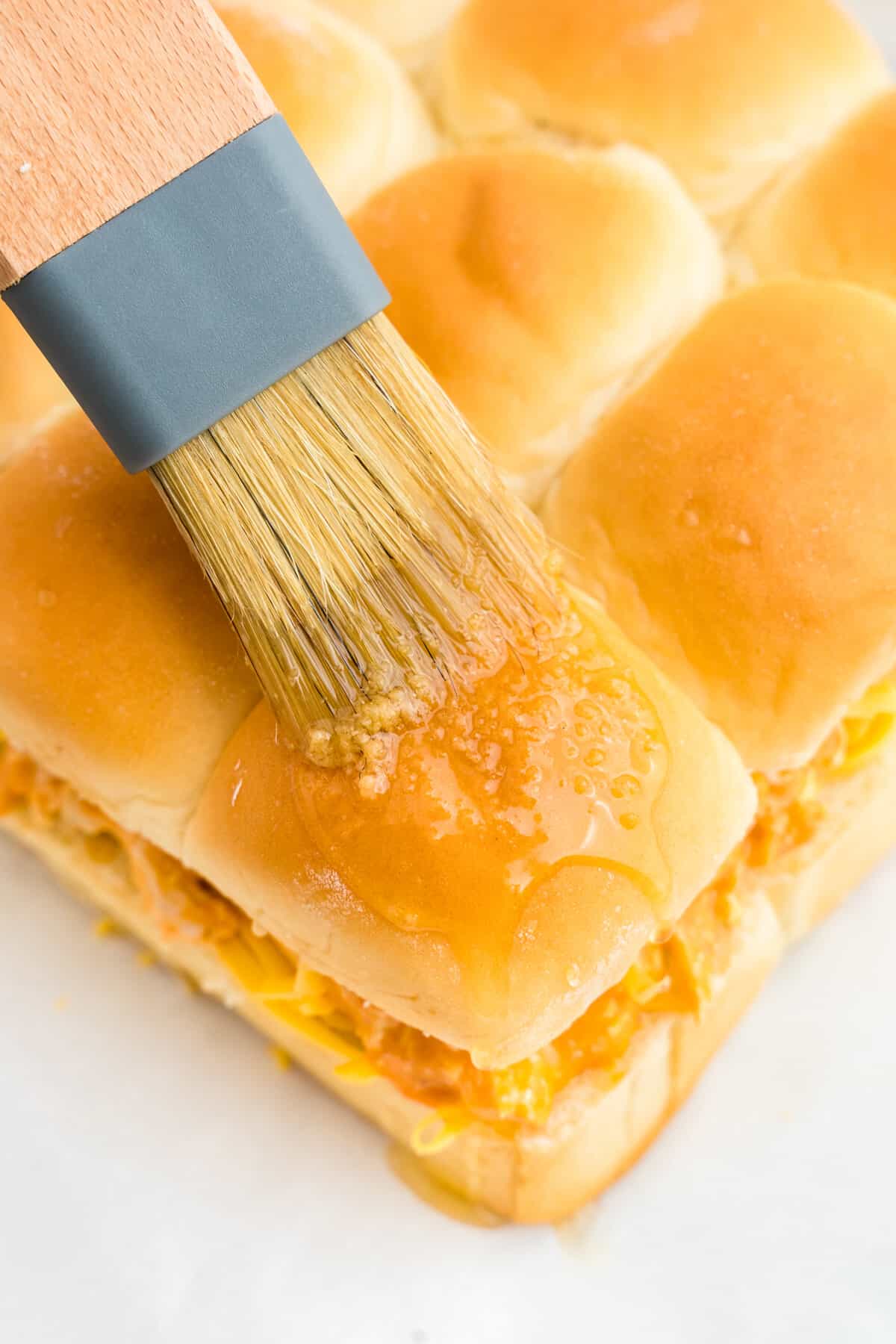 Brushing on butter to the tops of Hawaiian rolls for Buffalo Chicken Sliders 
