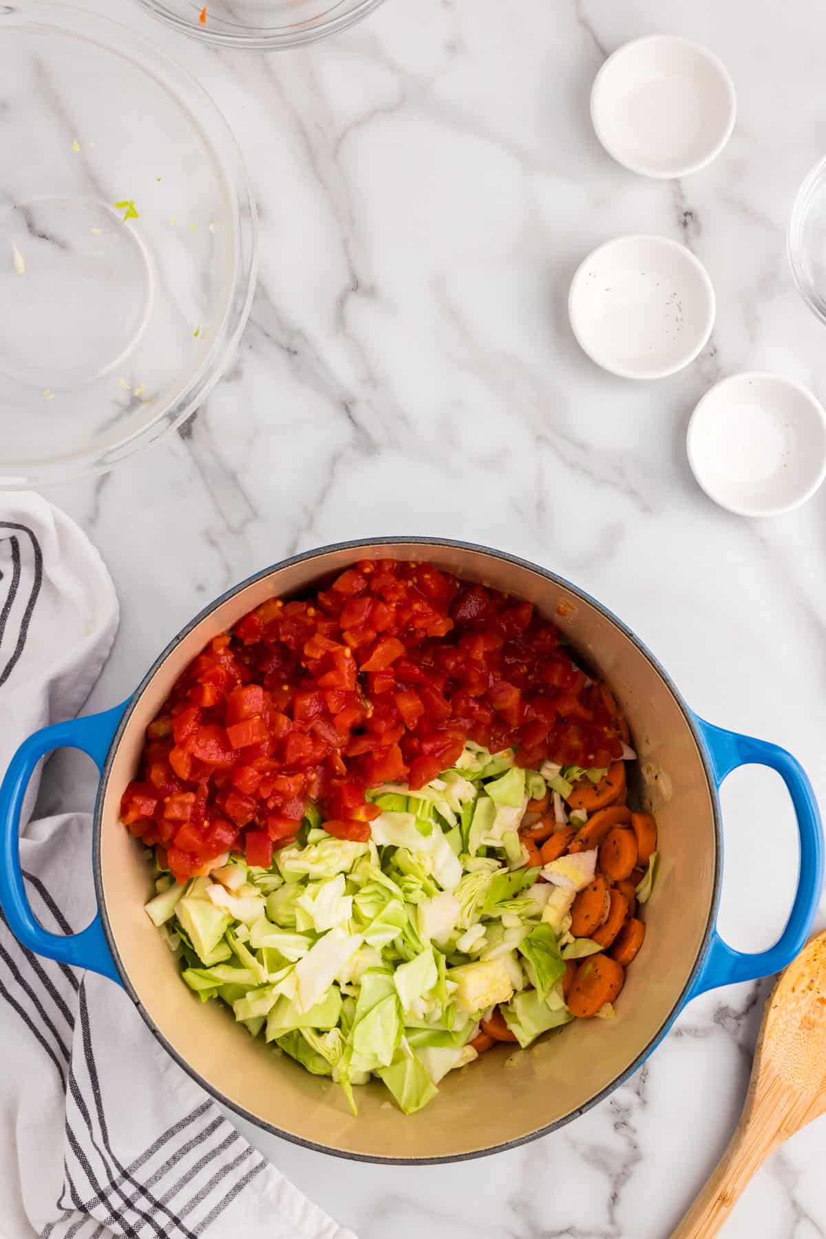 Adding chopped cabbage and diced tomatoes to Cabbage Soup mixture in Dutch Oven