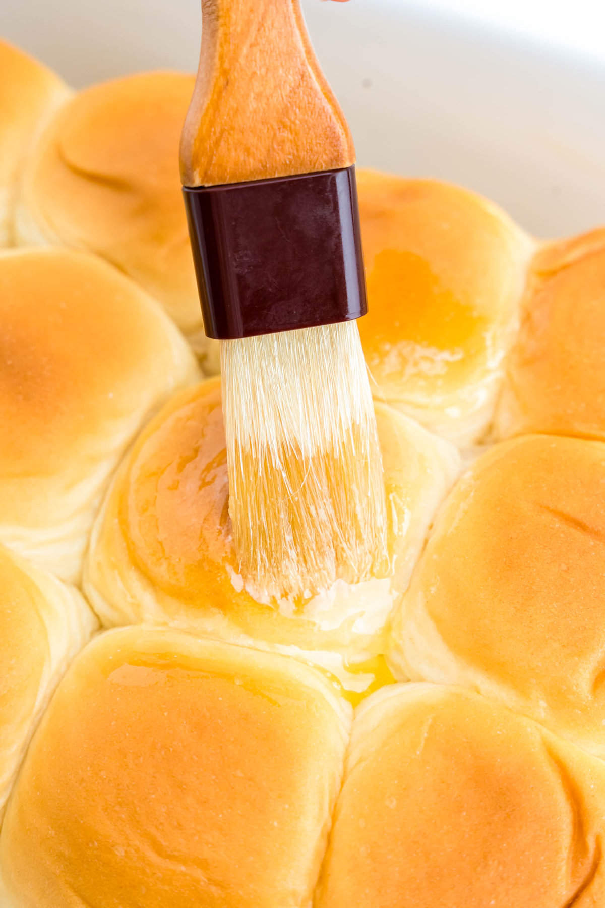 Brushing top of sweet rolls with unsalted butter for Cheeseburger Sliders recipe