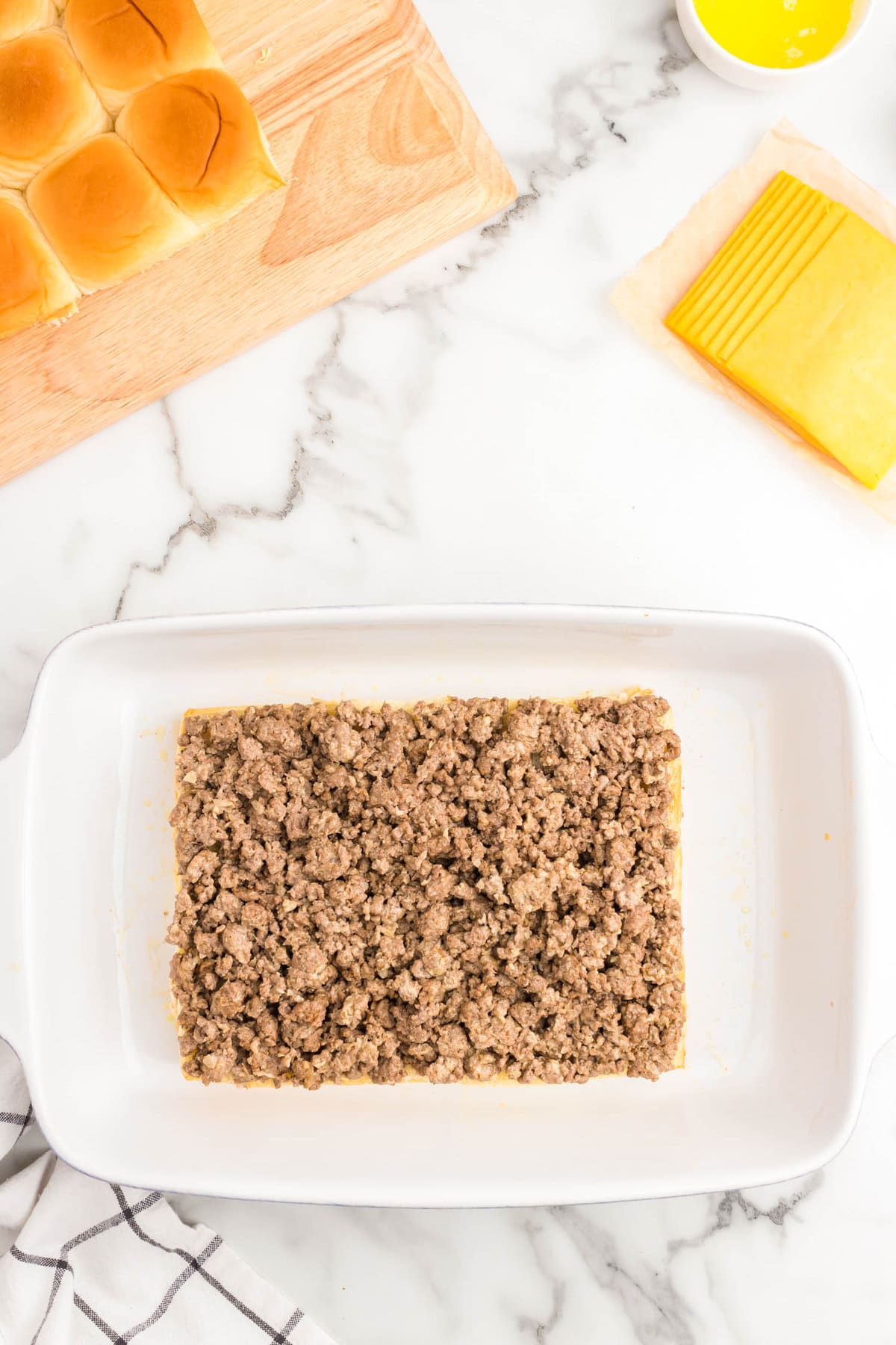 Adding seasoned ground beef to sweet rolls bottoms in baking dish for Cheeseburger Sliders Recipe