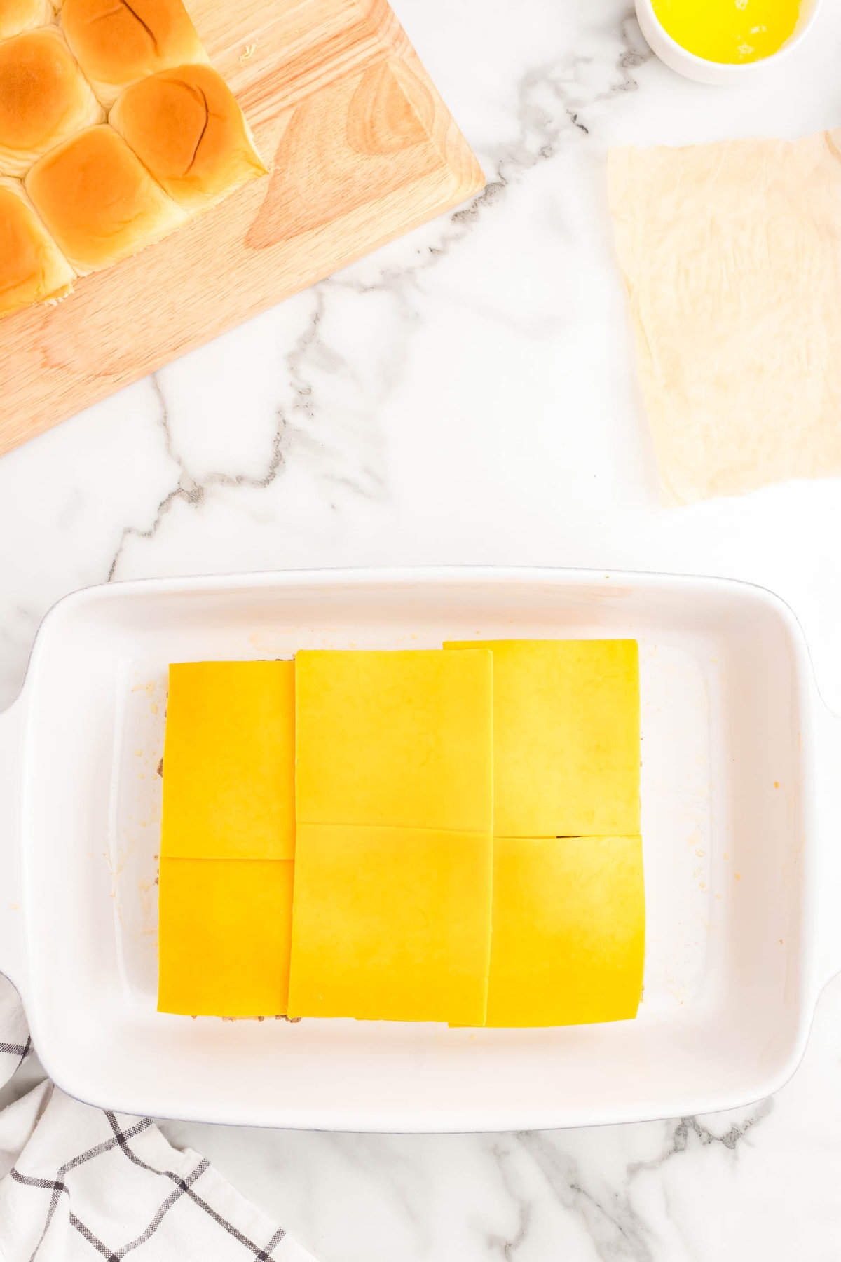 Topping ground beef with medium cheddar cheese for cheeseburger sliders with hawaiian rolls