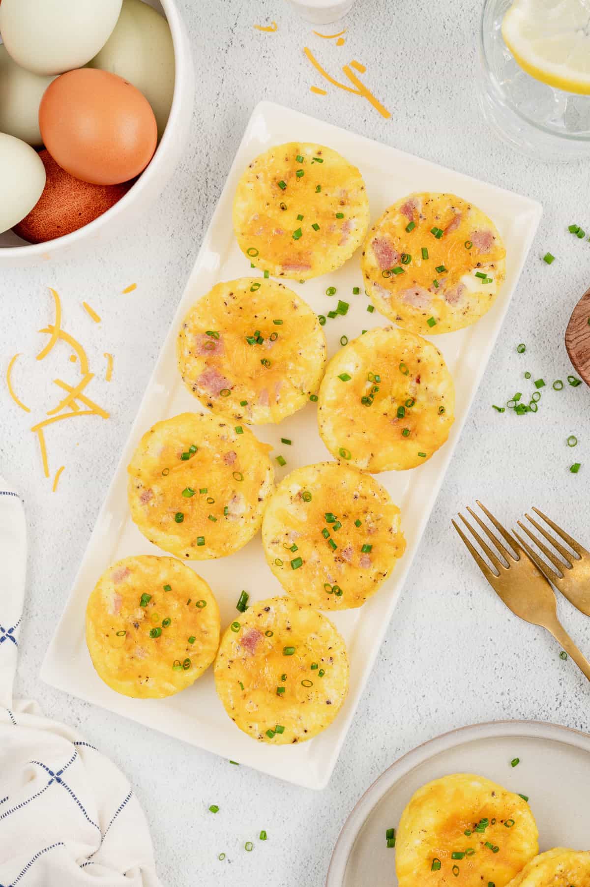 Breakfast Egg Muffins lined on serving plate topped with cheese and chives