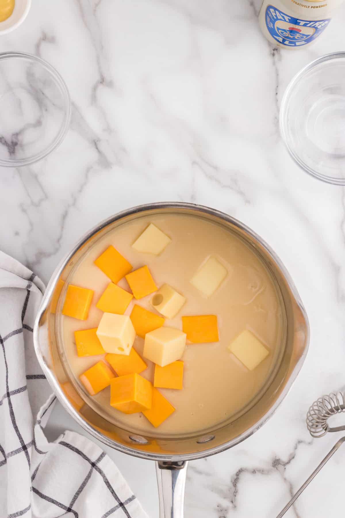 Adding cubed cheddar and swiss cheese to Beer Cheep Dip recipe in stovetop saucepan