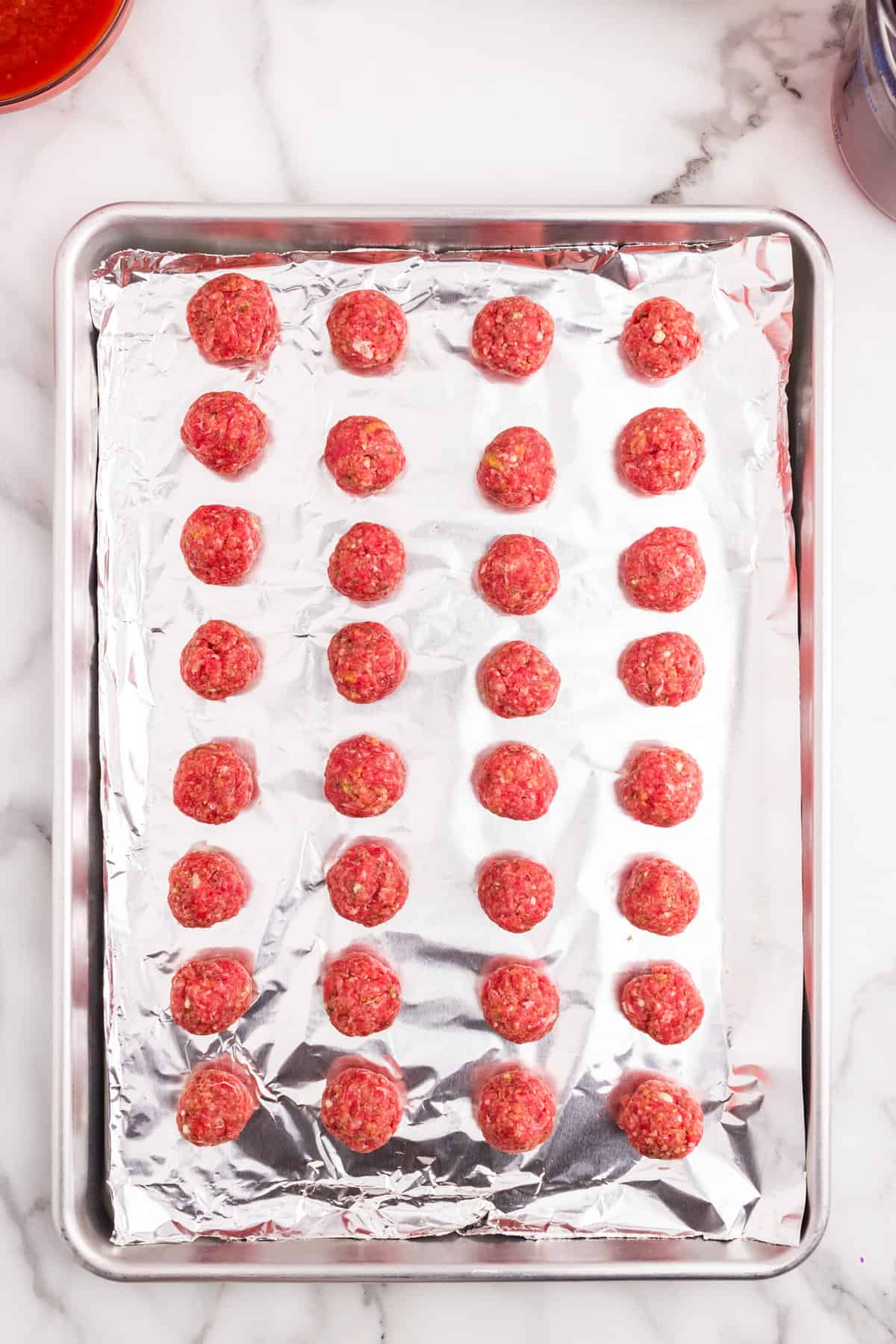 Mini meatballs formed into balls on tinfoil-lined baking sheet for Ground beef and seasonings in mixing bowl for meatballs for  Italian Meatball Soup recipe