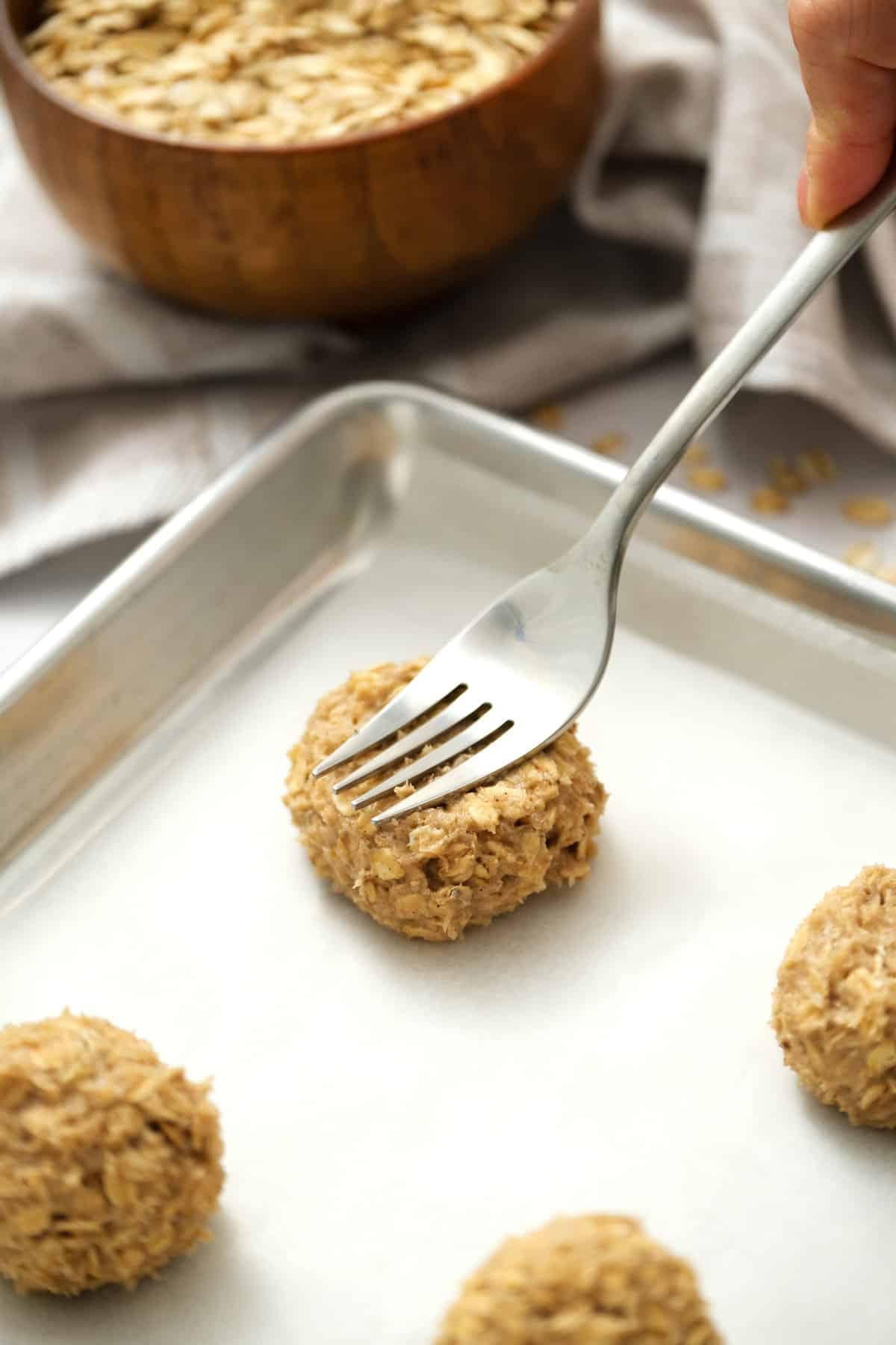 Fork pressing on oatmeal cookie on sheet pan