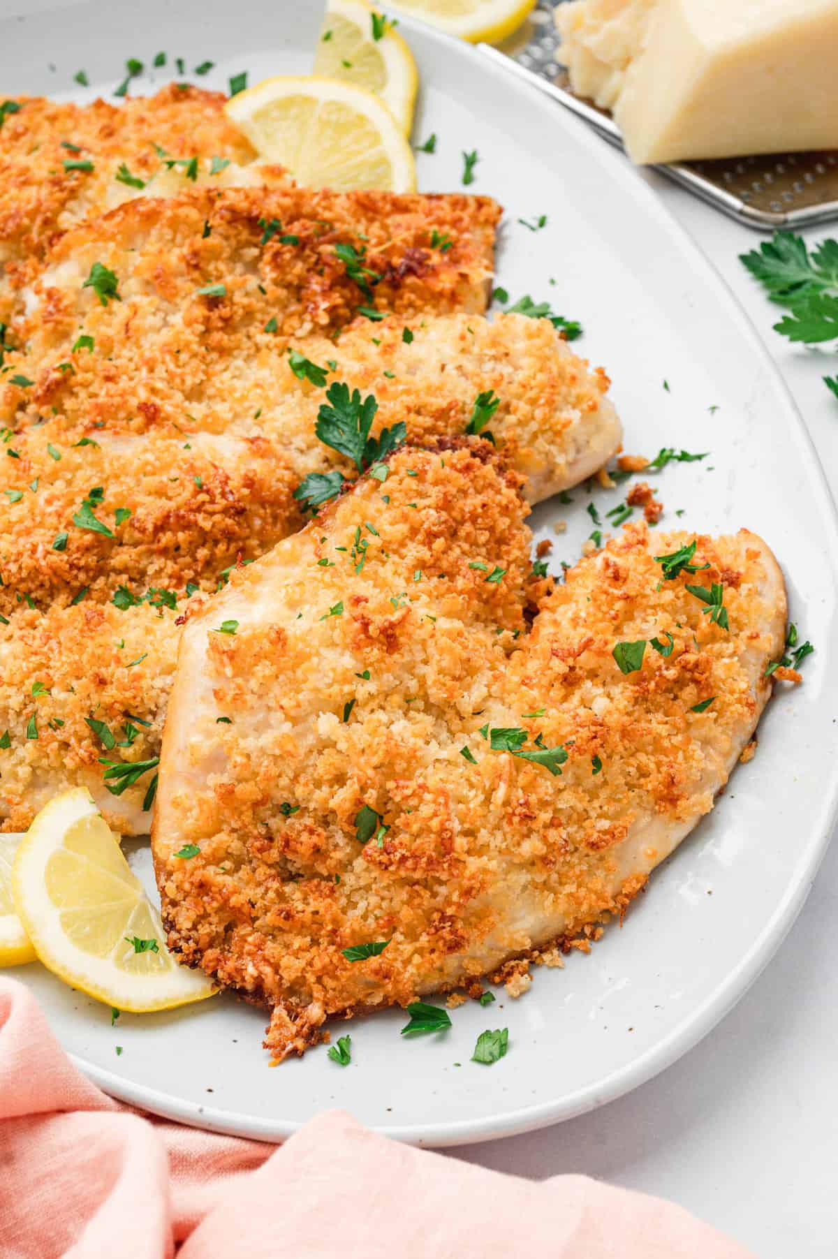 Parmesan Crusted Tilapia on serving plate topped with lemon wedges