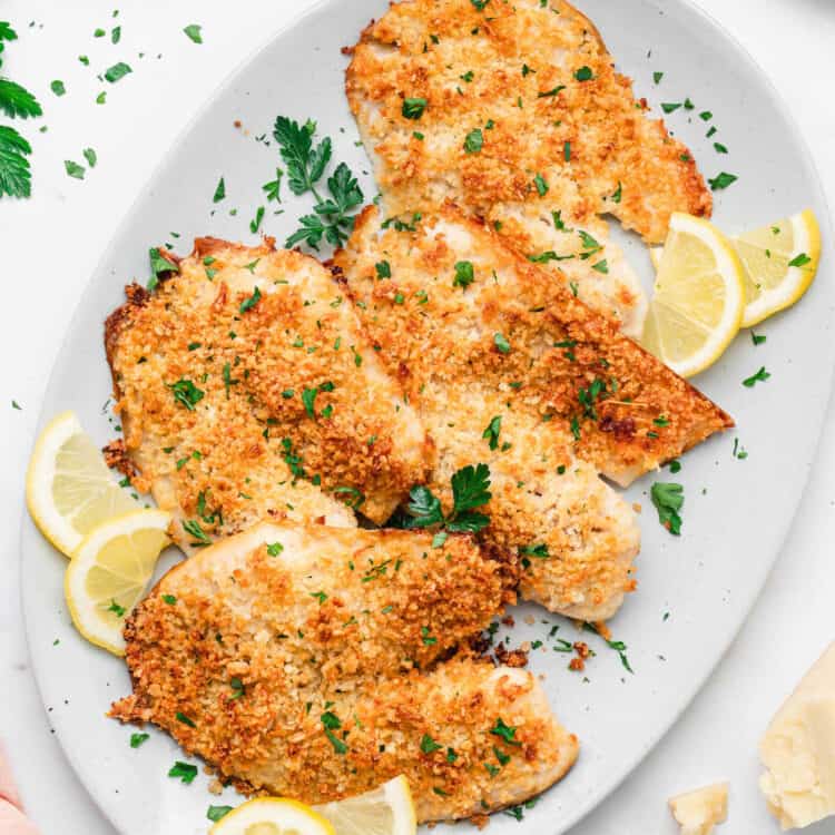 Parmesan Crusted Tilapia arranged on serving plate with lemon wedges