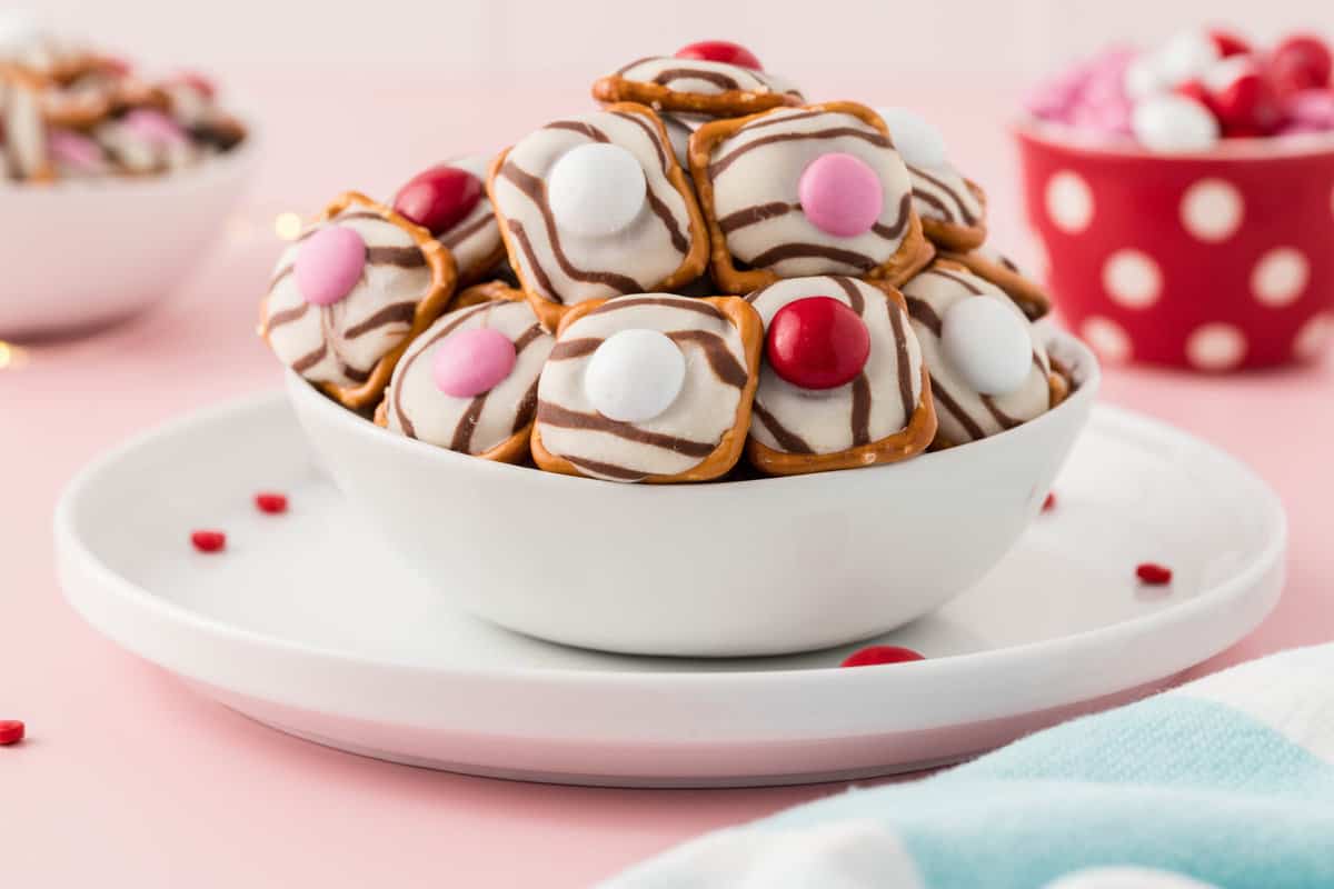 A White bowl full of Pretzels on top of a White Plate.