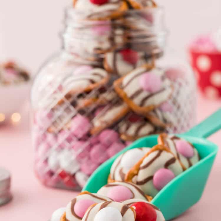 A Jar full of Pretzels with a scooper in front full of Pretzels also.