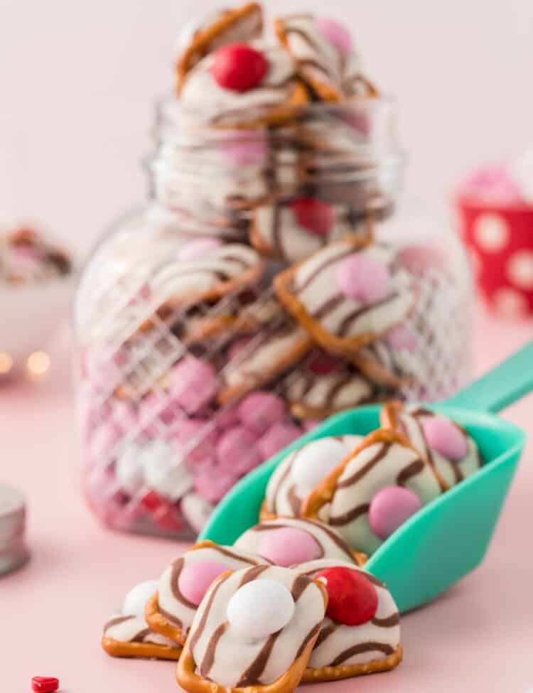 A Jar full of Pretzels with a scooper in front full of Pretzels also.