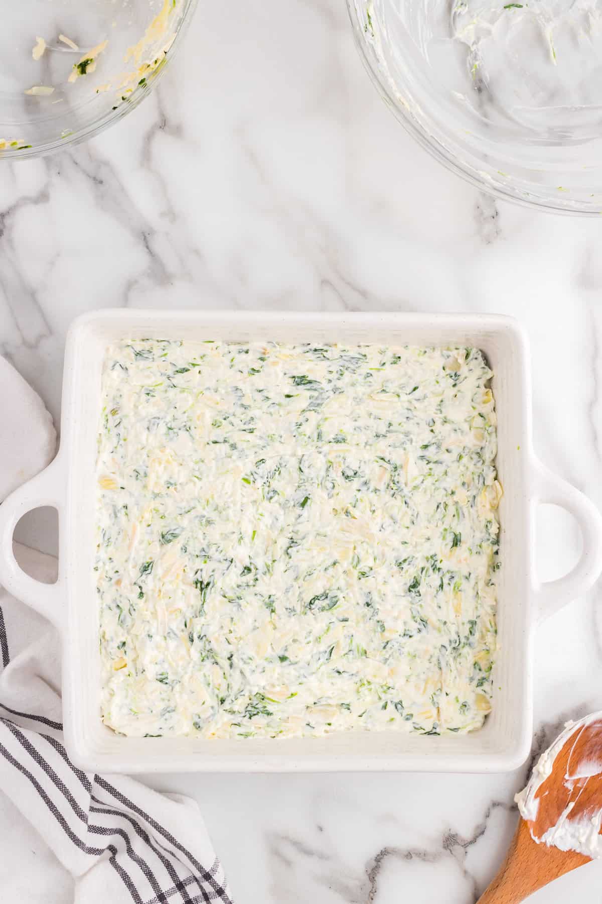 Spreading Spinach Artichoke Dip mixture in sqaure baking dish