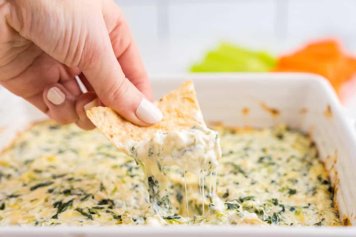 Spinach and Artichoke Dip in baking dish using a tortilla chip to scoop