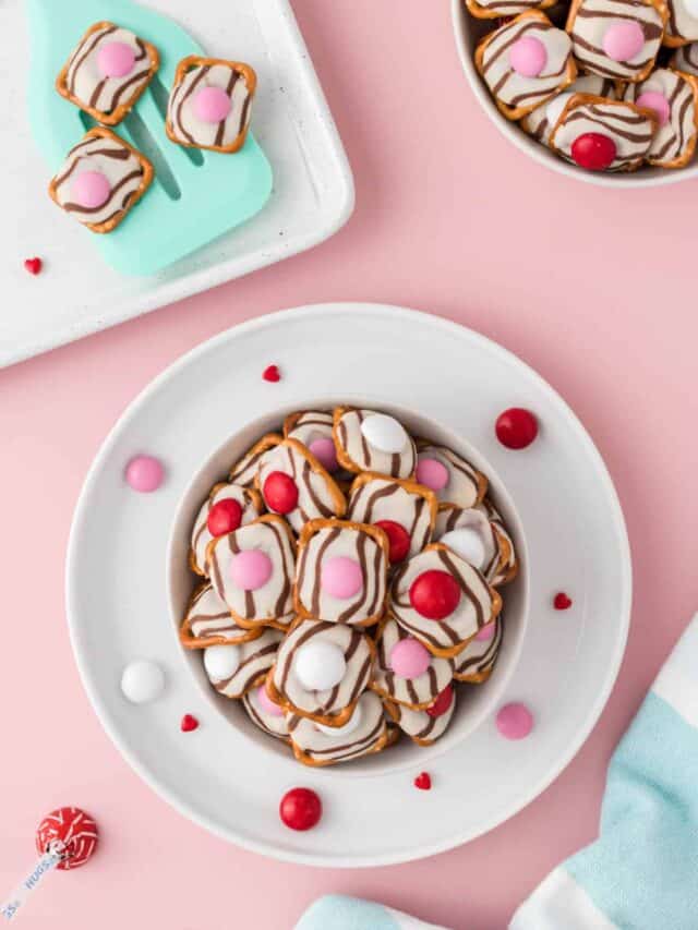 A White bowl full of Valentine Pretzel Hugs with a spatula in the corner with more pretzels on that.