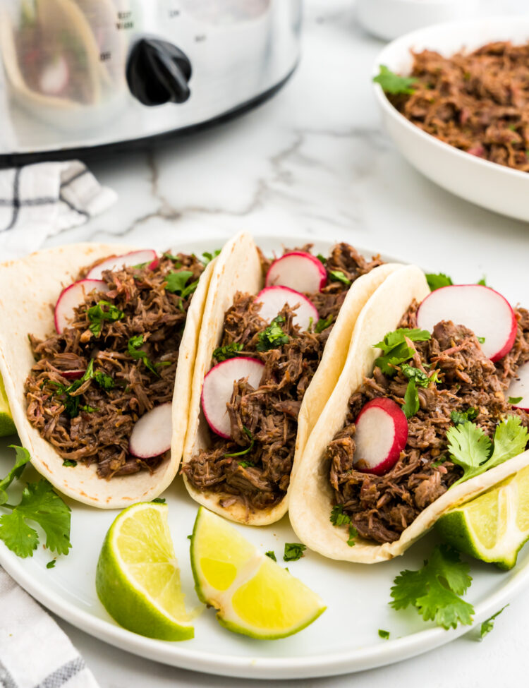 Barbacoa Beef in tortillas loaded with all the fixings on a plate