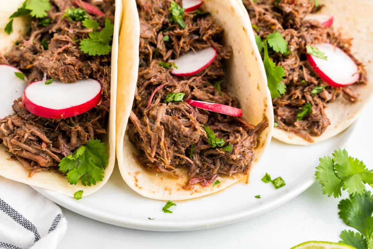 Barbacoa Beef in tortillas topped with all the fixings on a plate