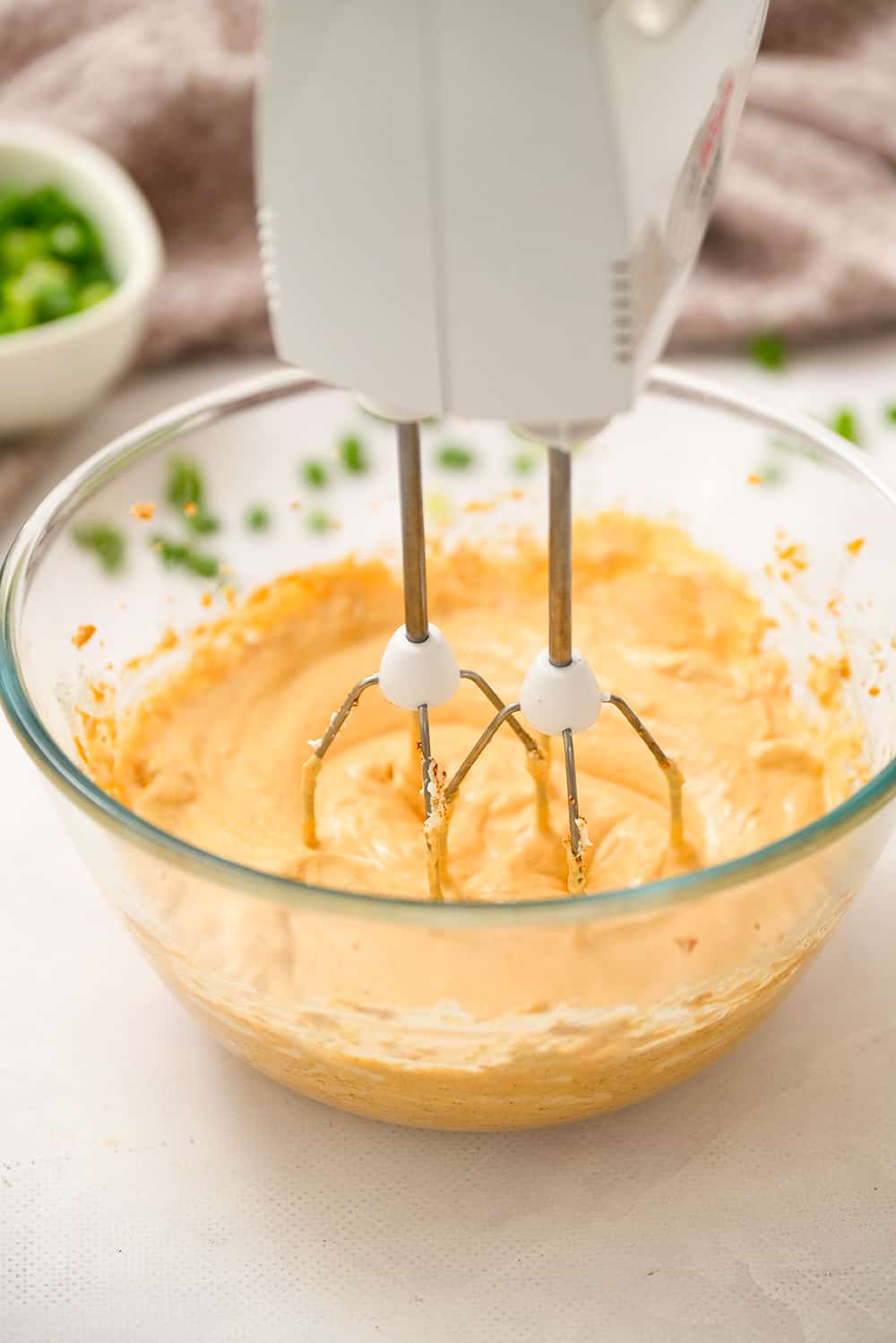 Hand mixer mixing taco dip ingredients in glass bowl