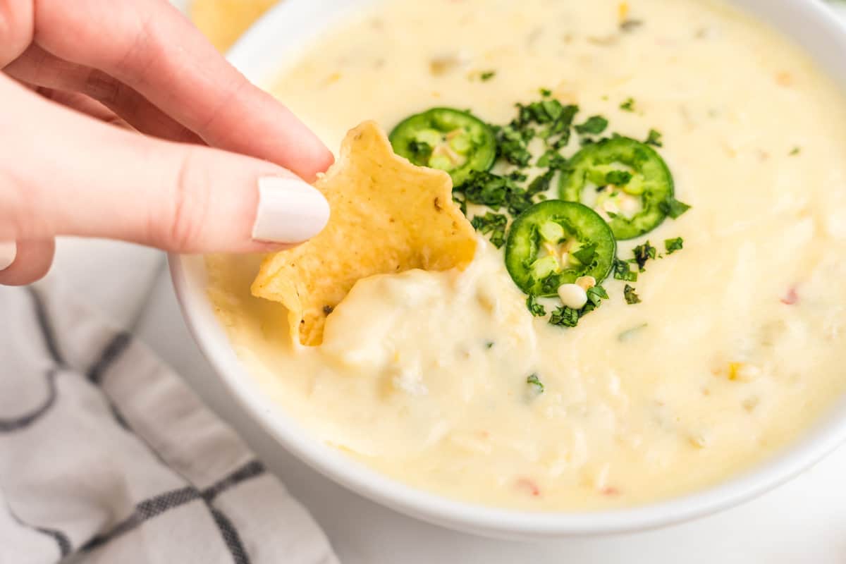 White Queso Dip in serving bowl using a tortilla chip for a dipper