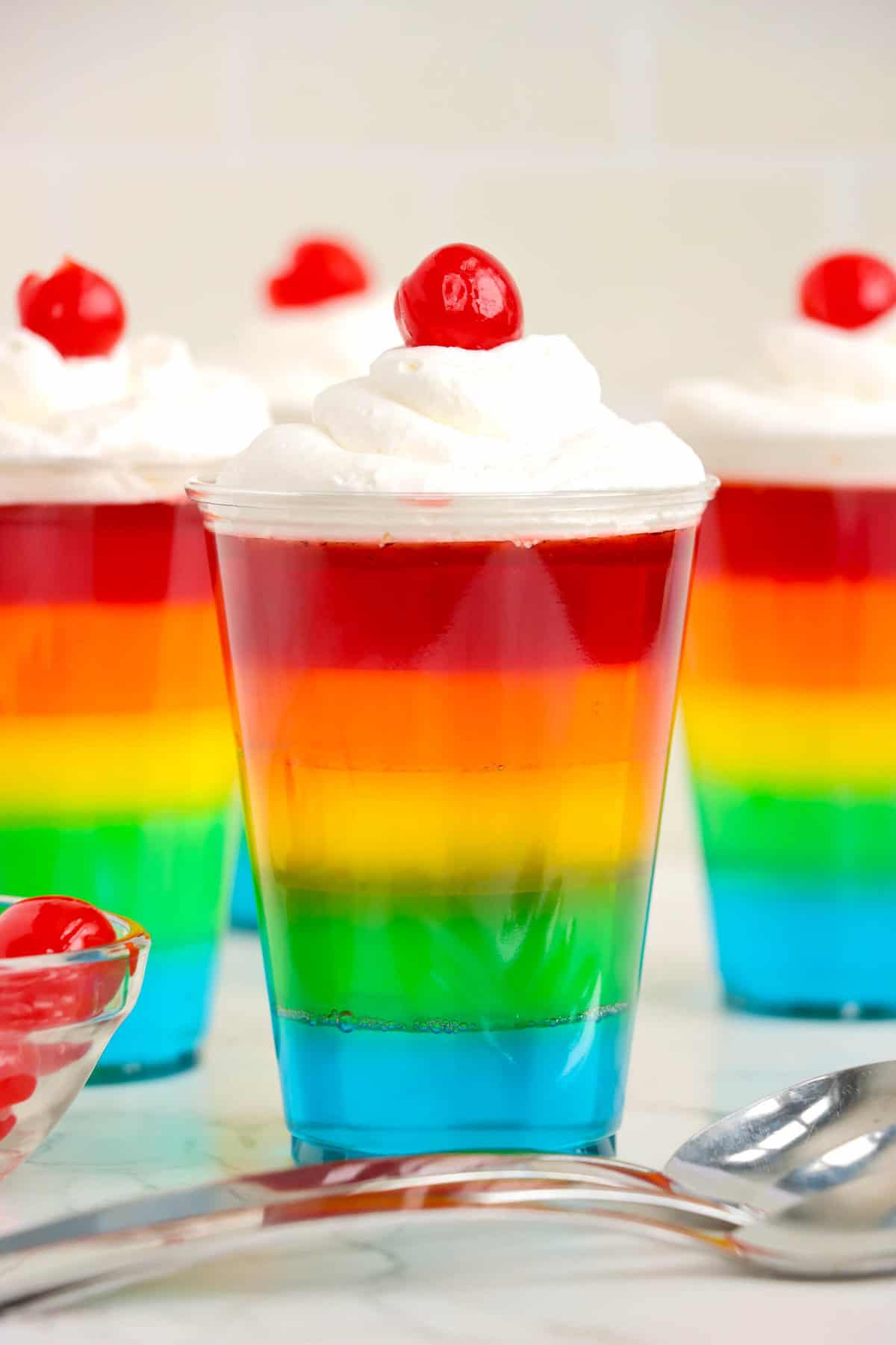 Photo of Rainbow Jell-O Cups with Whipped cream on top with a Cherry. 