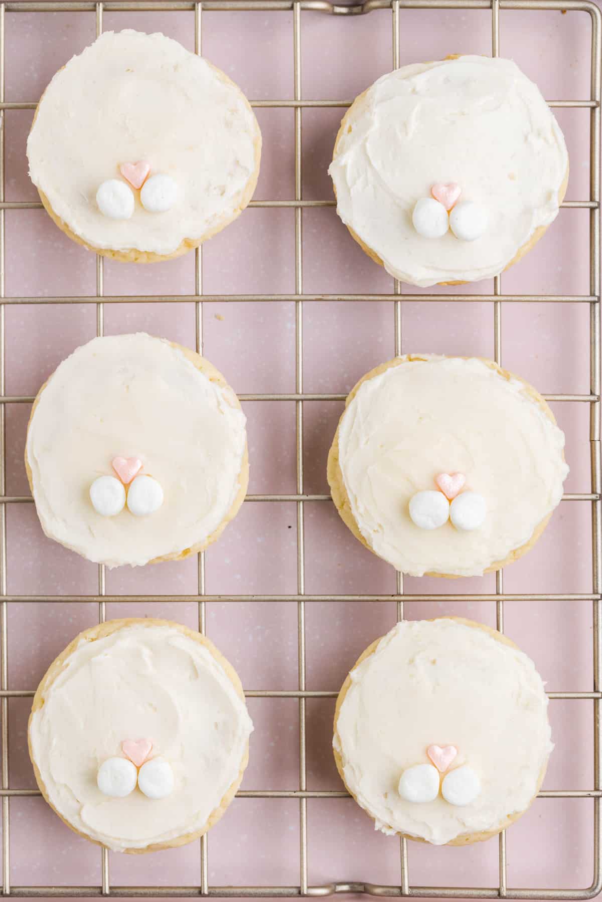 While frosting is still wet, place a heart shaped sprinkle in the center of the bottom of the cookie and add two halves of the mini marshmallows below the heart sprinkle.