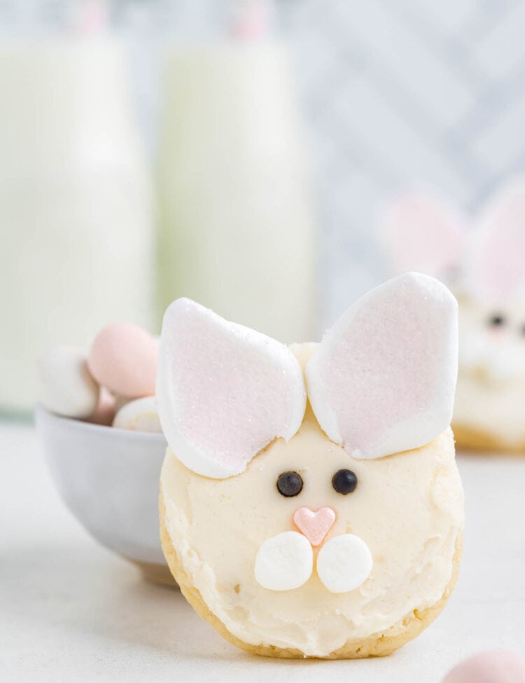 A Bunny Face cookie standing up right against a bowl filled with easter eggs.