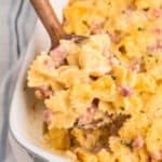 Closeup square image of Cheesy Ham Casserole in baking dish with wooden spoon