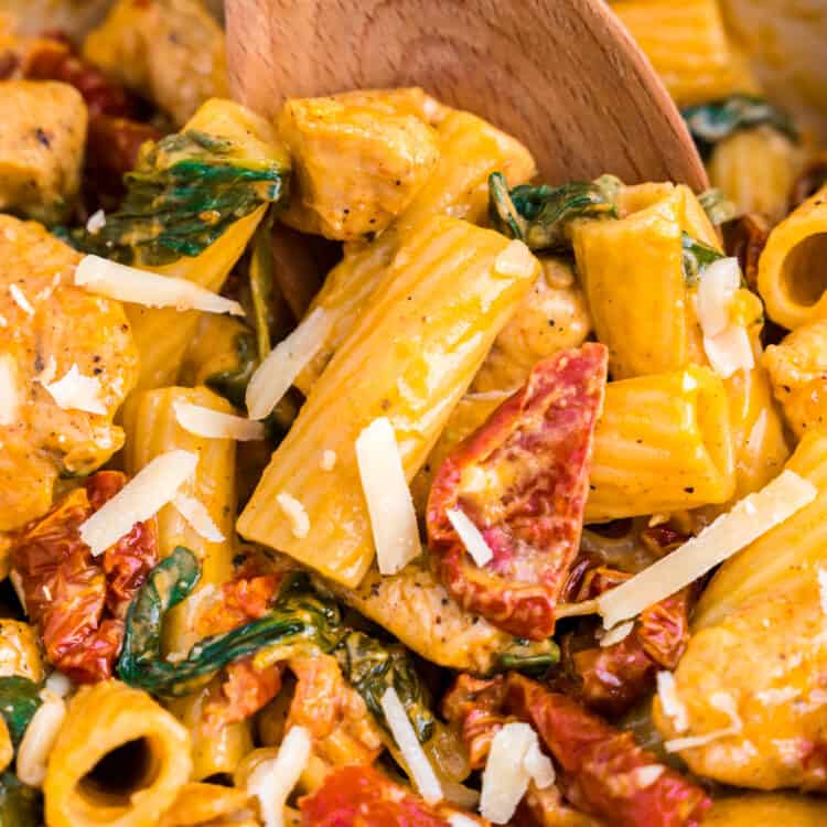 Creamy Tuscan Chicken Pasta being stirred with wooden spoon