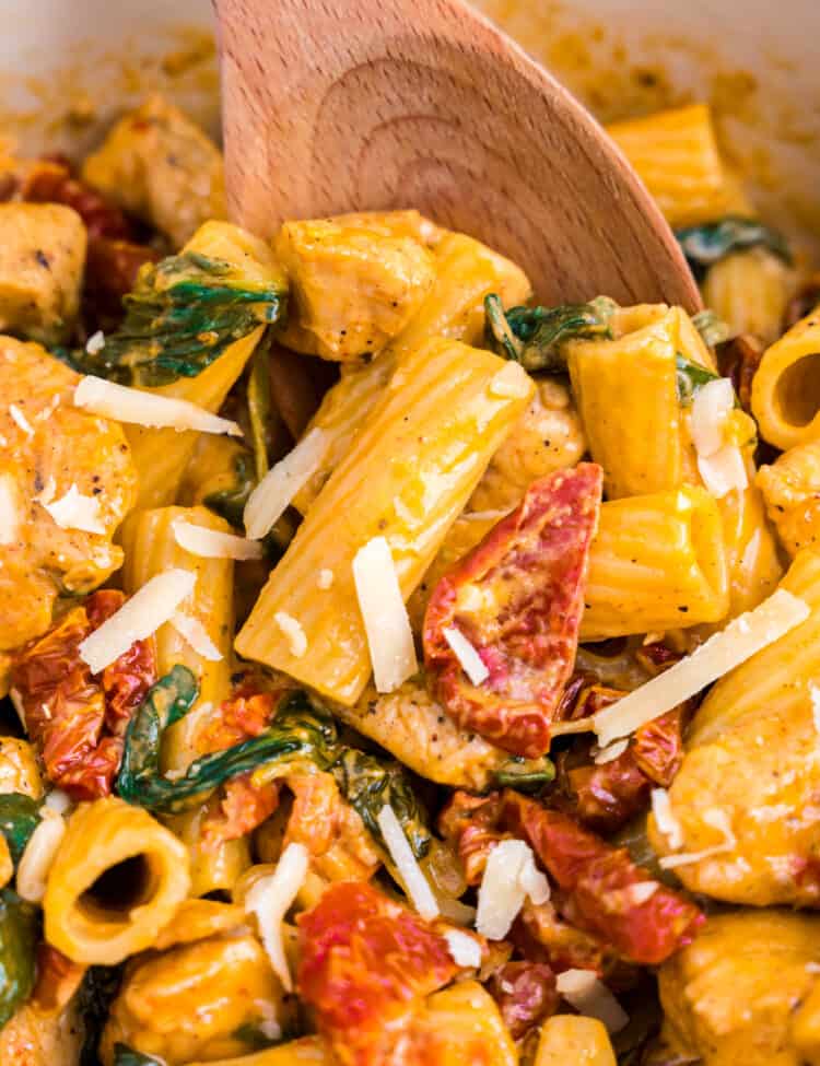 Creamy Tuscan Chicken Pasta being stirred with wooden spoon