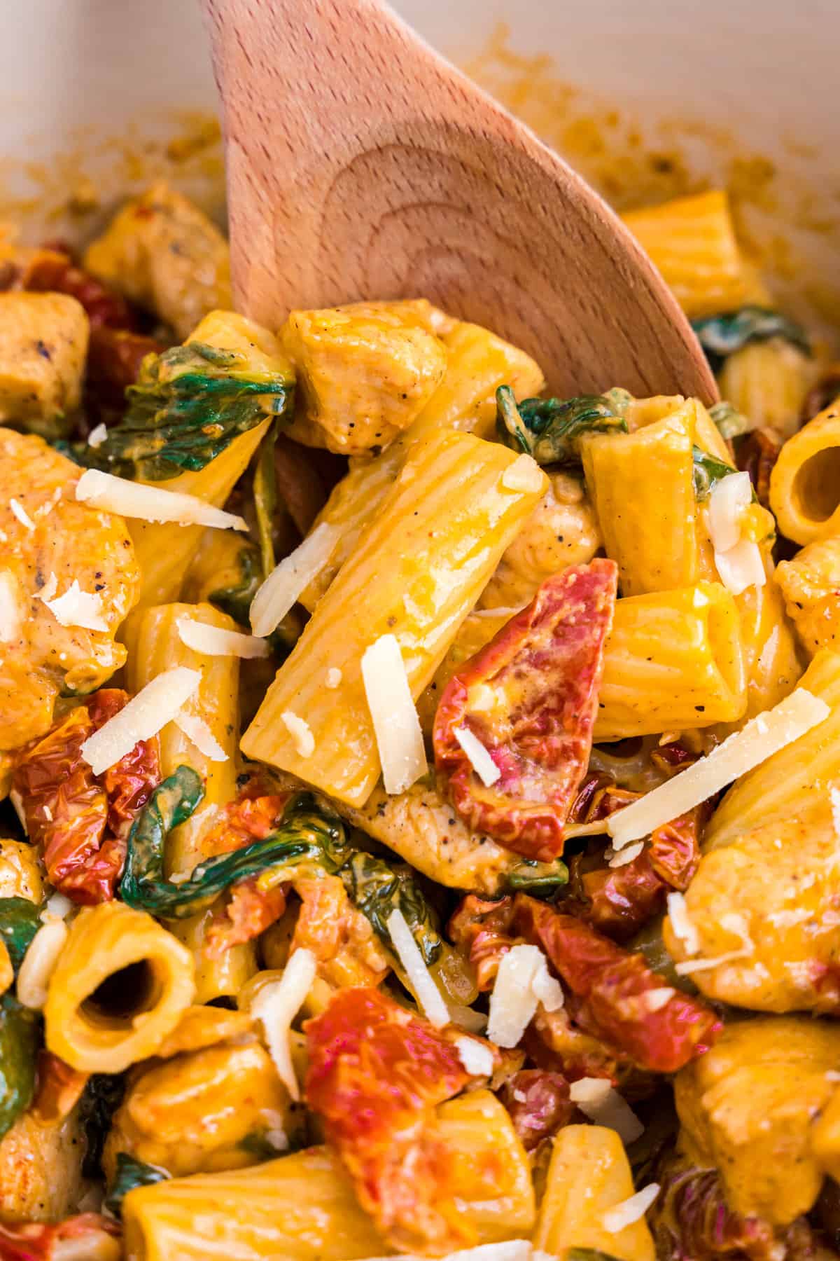 Creamy Tuscan Chicken Pasta being stirred with wooden spoon