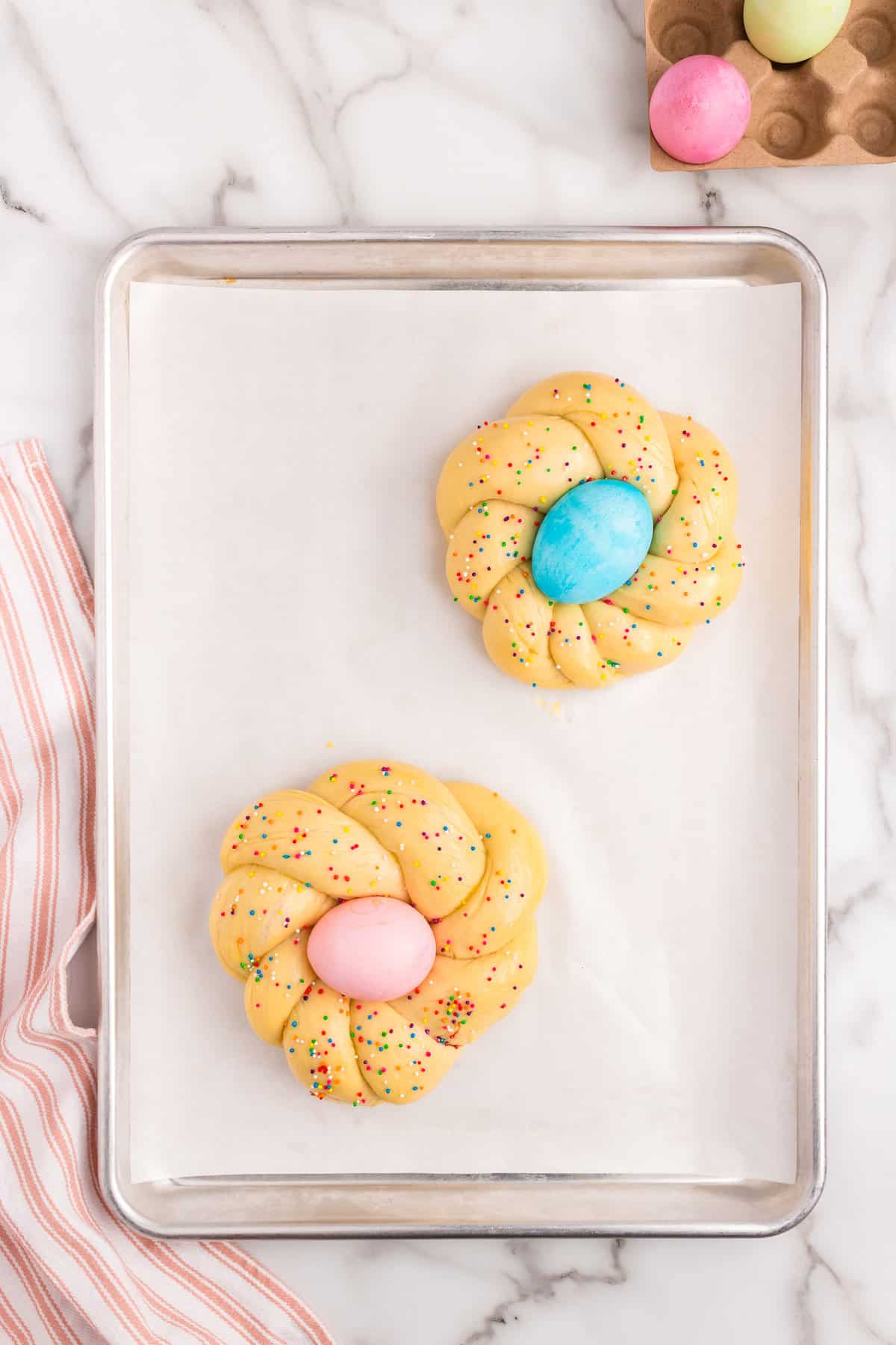 Placing dyed Easter Egg in Easter Bread and adding sprinkles on parchment-lined baking sheet