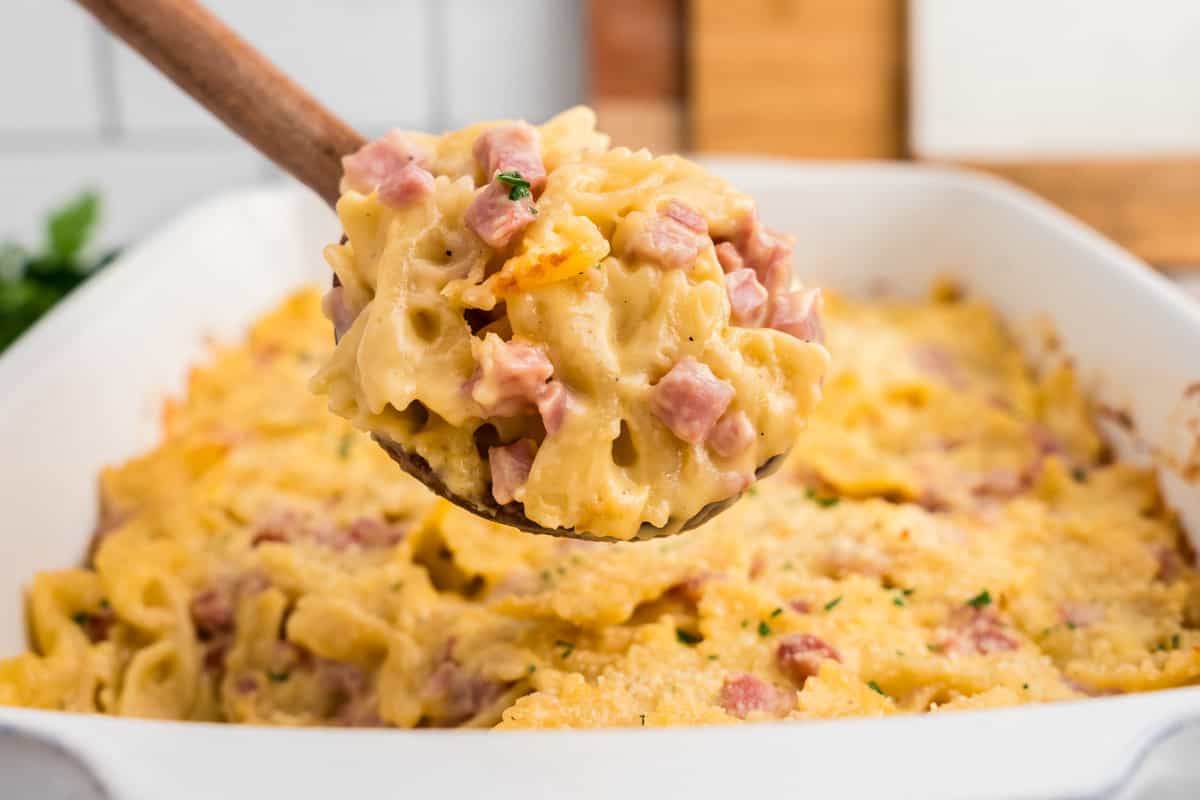 Using wooden spoon to scoop Cheesy Ham Casserole from baking dish