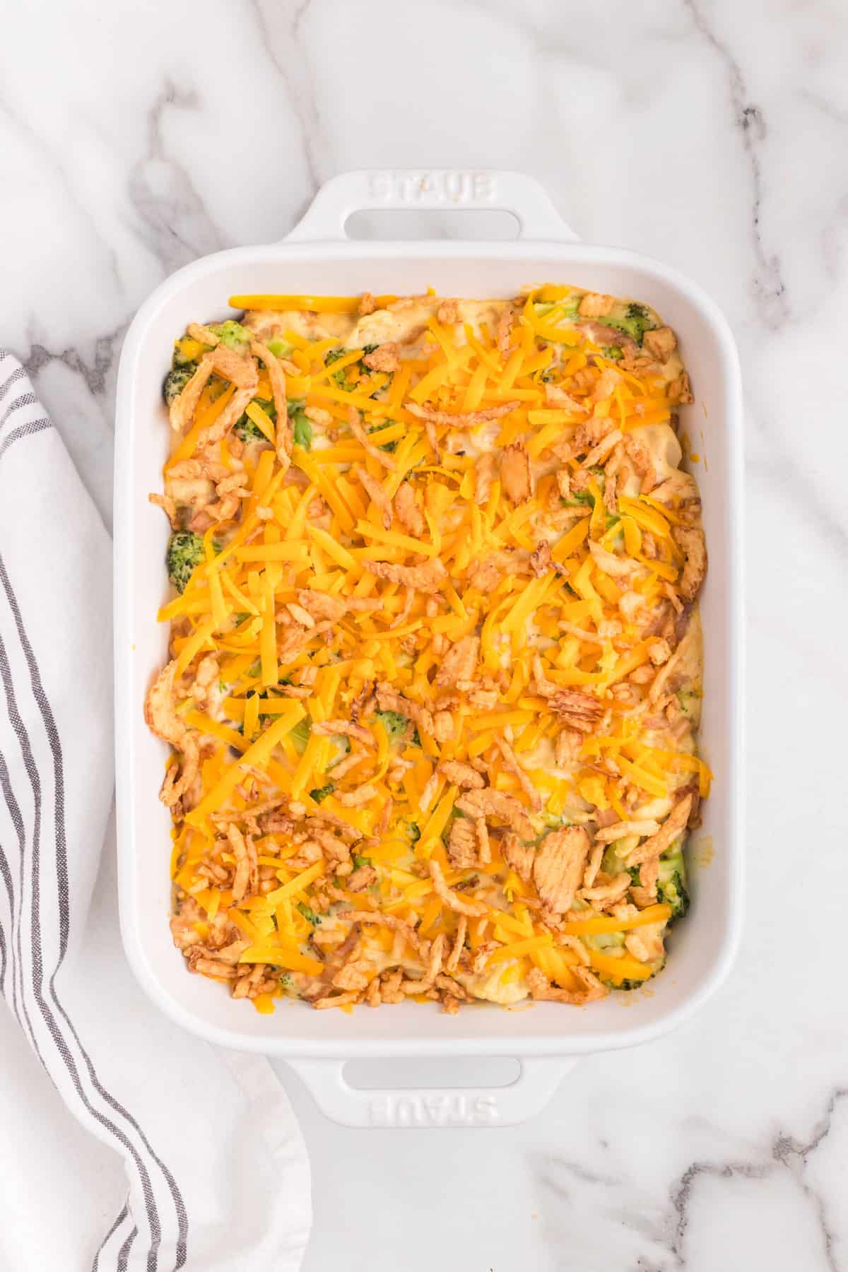 Topping Broccoli Cauliflower Casserole with shredded cheese and french fried onions