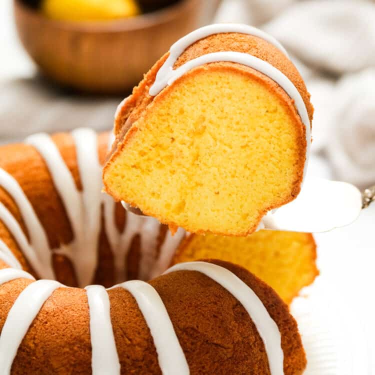 Lemon Bundt Cake with glaze on serving plate with one slice cut and being removed