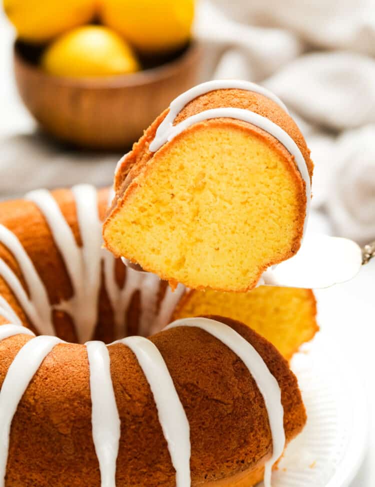 Lemon Bundt Cake with glaze on serving plate with one slice cut and being removed