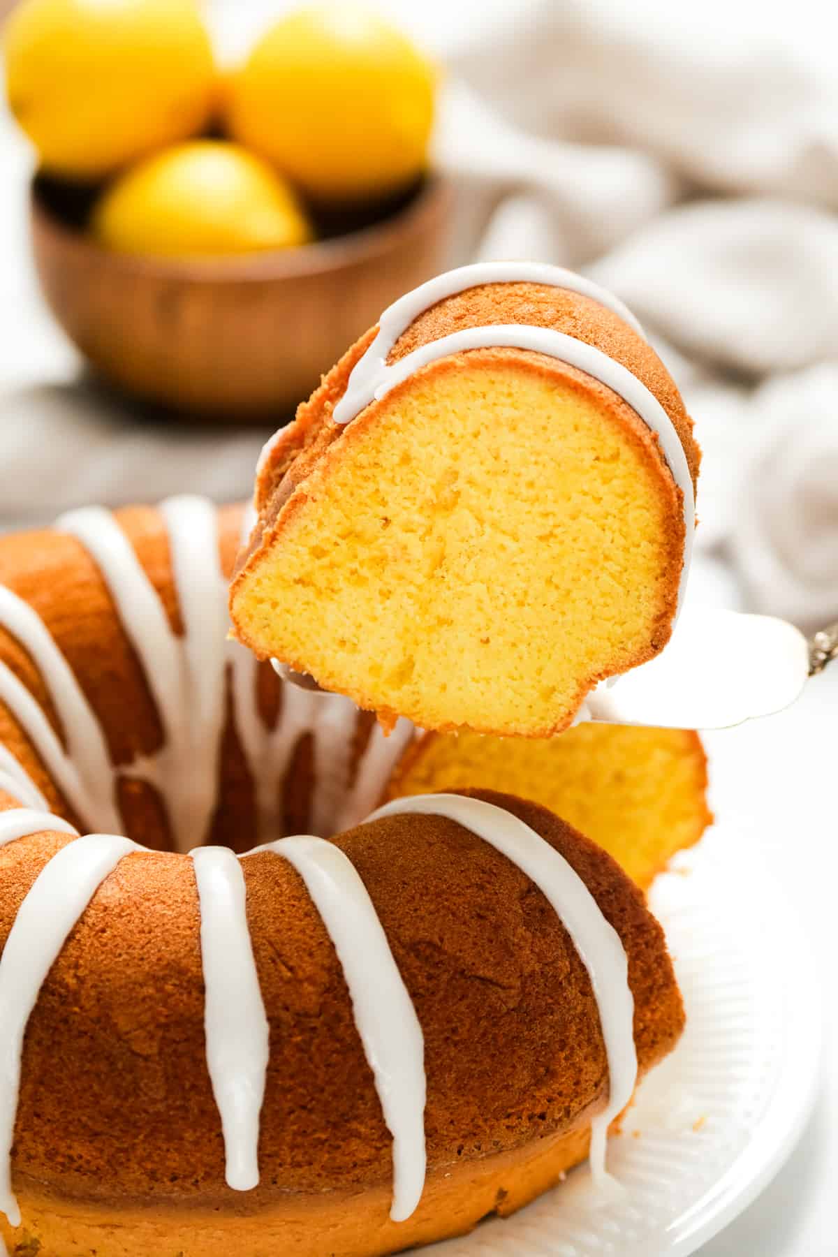 Lemon Bundt Cake with glaze on serving plate with one slice cut and being removed