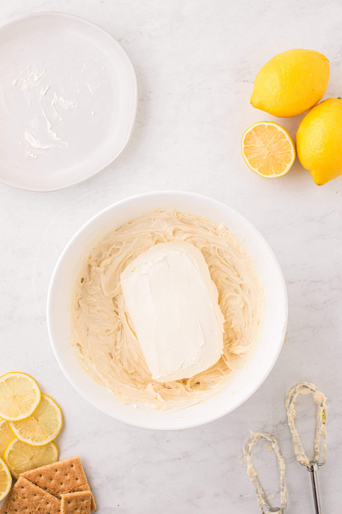 Adding softened cream cheese block to mixed Lemon Cheesecake ingredients