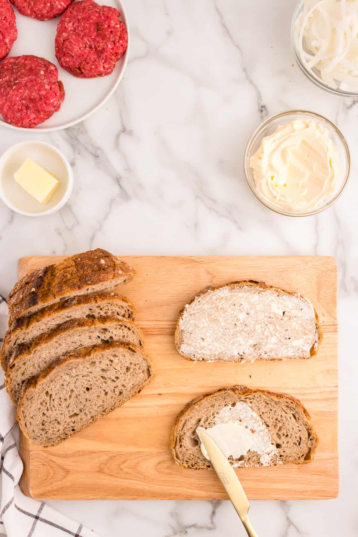 Spreading mayo on rye bread on a wooden cutting board for Patty Melt recipe