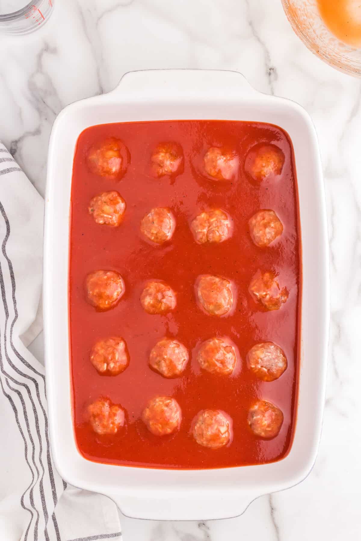 Pouring sauce over formed meatballs in 9x13 baking dish for Porcupine Meatballs recipe