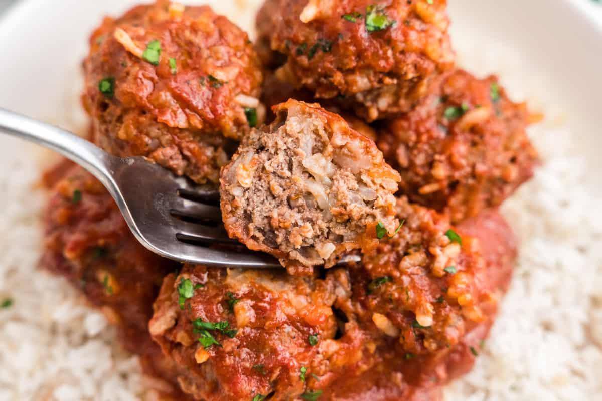 Using a fork to take the first bite of a Porcupine Meatball atop a bed of rice