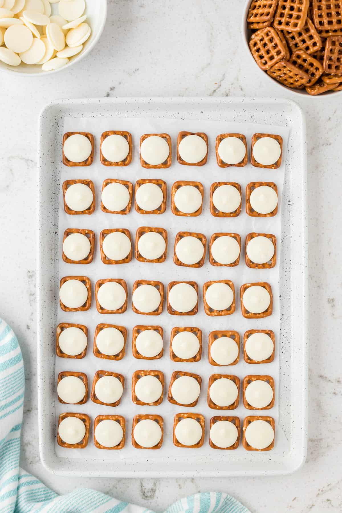 Next, place a white candy melt on each of the pretzels. Place them into the oven and melt them slightly.