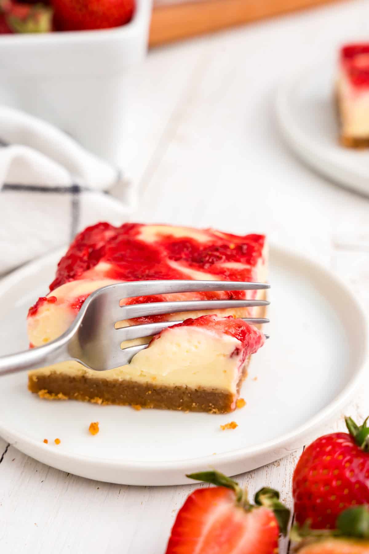 Strawberry Cheesecake Bars cut into square on plate and using a fork to take the first bite