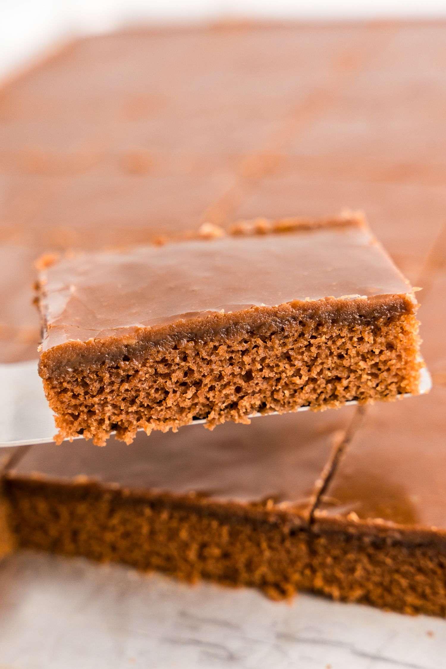 Texas Sheet Cake cut into squares and using spatula to remove a piece from pan