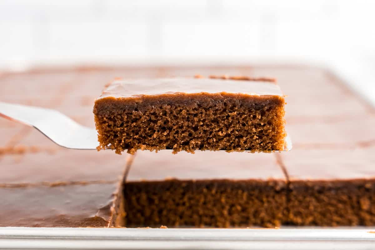 Texas Sheet Cake cut into squares and using spatula to remove a piece from pan